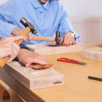 Metalltreiben ©Manfred Rauscher 2018 Kinderhände, die mit Hämmern eine Kupferplatte auf einem Holzstock bearbeiten.